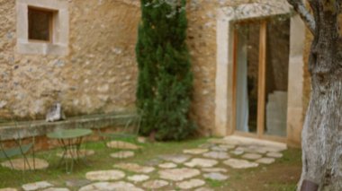 Taş duvarları, yeşil bahçe mobilyaları ve sakin bir açık hava ortamını yakalayan bir ağaç olan eski bir Akdeniz evinin bulanık görüntüsü..