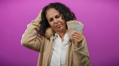 Romanyalı banknotları tutan orta yaşlı bir kadın canlı mor bir geçmişe karşı kafa karışıklığı göstererek, mali belirsizliği öne sürüyor.