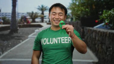 Şehir sokağında yeşil kurdele tutan genç bir adam, gönüllü tişört giyiyor, şehir ortamında ve Çin 'de toplum içinde yer almayı sembolize ediyor..