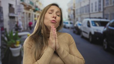 Yoğun bir şehir sokağında gözleri kapalı dua eden bir kadın, açık şehir ortamında duygu ve umut gösteriyor..