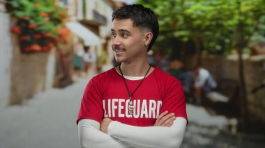 Kırmızı bir cankurtaran gömlekli genç İspanyol adam canlı bir şehir caddesinde çapraz kollarıyla duruyor, canlı şehir ortamına karışıyor, yaz havası yayıyor..