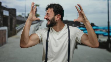 Hispanik sakallı bir adam duygusal olarak deniz kenarında bir gezinti yapıyor. Arka planda deniz ve deniz var..