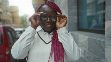 Şehir sokaklarında gülümseyen gözlüklü bir kadın şehrin atmosferini yansıtıyor stil güveninin ve modern yaşam tarzının özünü yakalıyor..