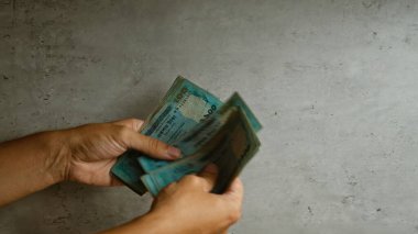 Finansal işlemleri gösteren somut bir arkaplan karşısında banknotları sayan eller