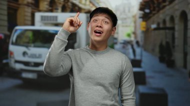 Gri kazaklı genç Çinli adamın taksilerle ve arka planda insanlarla dolu bir caddede parlak bir fikri var..