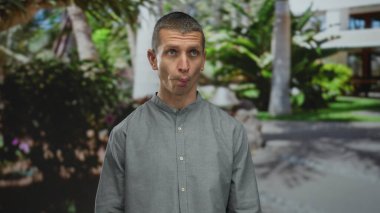 Parktaki yeşil ve modern binalarla çevrili komik suratlı adam, parlak güneş ışığı altında neşeli ve rahat bir atmosfer yaratıyor..