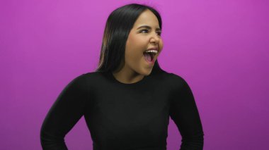 İzole edilmiş pembe bir arka plan karşısında coşkuyla gülen genç Latin kadın neşeli bir ifade ve canlı bir kişilik sergiliyor..