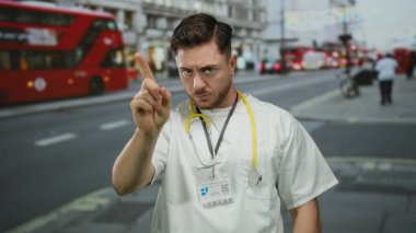Sakallı genç doktor, şehrin arka planında kırmızı çift katlı otobüsleri gösteriyor, steteskop takıyor, sağlık bilincini veya tıbbi konsepti resmediyor..