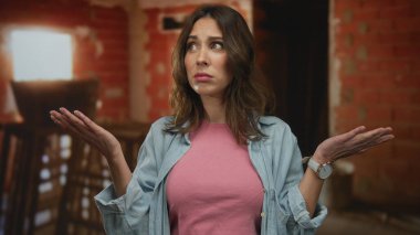 İnşaat alanındaki İspanyol kadın pembe gömlekli mavi ceketli, belirsiz bir ifadeyle gündüz vakti şehir merkezindeki tamamlanmamış bina geçmişini sorguluyor..