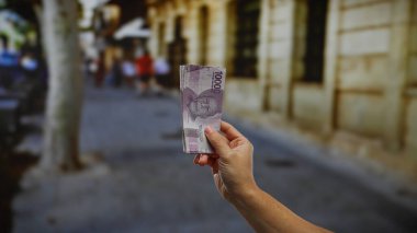 Endonezya 'nın şehir sokağında banknotları elinde tutan adam, hareketli şehir ortamında para değişimi sergiliyor..