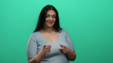 Uzun saçlı gülümseyen kadın yeşil arka planda şakacı bir şekilde giyiniyor..