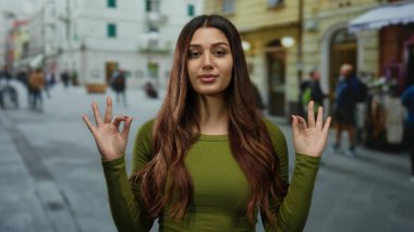 Kalabalık bir caddede, gözleri kapalı meditasyon yapan, şehir manzarasının ortasında sakinlik ve rahatlık saçan, canlı bir şehir ortamında dinginlik ve farkındalık sergileyen bir kadın..
