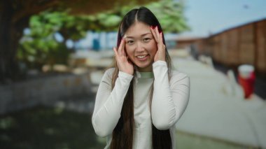 Güneşli bir şehir caddesinde gülümseyen bir kadın neşeli bir ifadeyle ve şık uzun saçlarıyla açık havada enerjik bir hava sergiliyor..