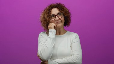 Çenesi dinlenmiş bir kadın canlı pembe bir duvarın önünde düşünceli bir ifade takınıyor.