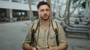 Elinde kamera olan beyaz sakallı genç bir adam şehir sokağında fotoğraf çekimi için bekliyor. Sırt çantası takıyor ve turist gibi görünüyor..