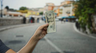Bir şehir caddesinde bir Amerikan doları banknotunu tutarken arka planda bulanık bir şehir manzarası yakalıyorum..