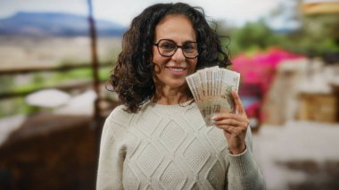 Güneşli bir restoran terasında Rus rublesi tutan bir kadın, açık havada finansal başarı ve rahatlama öneriyor..
