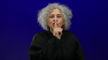 Gri saçlı yaşlı kadın, izole edilmiş mavi bir arka plana karşı sessizliğini koruyor. Huzur ve sükuneti iletiyor..