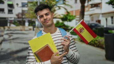 Şehir caddesinde elinde klasörler ve İspanyol bayrağı olan bir adam mutlu bir şekilde eğitim ve uyruğunu gelişigüzel bir şehir ortamında temsil ediyor..