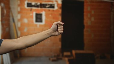 Kapalı bir inşaat alanının ön planında yumruğunu sıkmış bir adamın kolu tuğla duvarların ve dağınık aletlerin arasında, ev yenileme işi olduğunu gösteriyor..