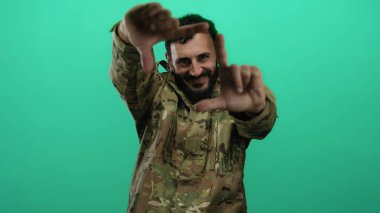 Askeri üniformalı İspanyol bir adam yeşil arka planda poz veriyor ve elleriyle bir çerçeve oluşturuyor..