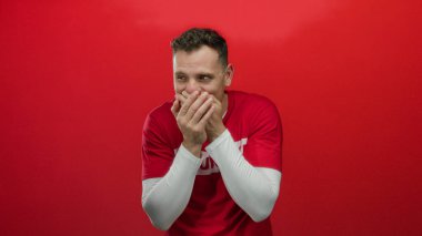 Kırmızı gönüllü gömleği giyen adam kırmızı arka plana karşı coşkuyla tepki veriyor, sürpriz ve mutluluk taşıyor.