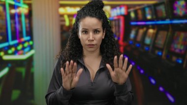 Genç İspanyol kadın, arka planında renkli kumar makineleri olan canlı bir kumarhanede sakin bir şekilde el kol hareketi yaparak heyecanın ortasında sükunet duygusunu iletiyor..