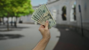 Bir şehir caddesinde elinde Amerikan doları banknotları tutan beyaz erkek eli ve para birimine odaklanmış finansal zenginlik sergiliyor..
