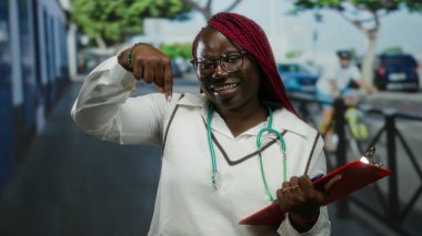 Kadın doktor elinde bir not panosuyla şehir sokaklarında gülümsüyor ve boynunda steteskopla neşeli ve olumlu tavırları vurguluyor.