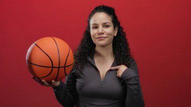 Elinde basketbol topu tutan kadın kırmızı arka planda kendine güvenini ve kararlılığını gösteriyor..