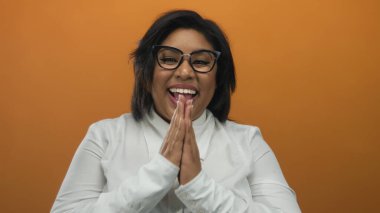 Turuncu arka planda sevinçle gülümseyen gözlüklü ve beyaz gömlekli bir kadın, izole edilmiş canlı bir stüdyoda mutluluk ve pozitifliği ifade ediyor..