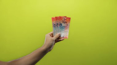 İzole edilmiş sarı arka planda İsviçre frangı banknotları tutan bir adamın eli, İsviçre 'den net ve canlı bir yakın çekim görüntüsü gösteren renkli bir para birimi..