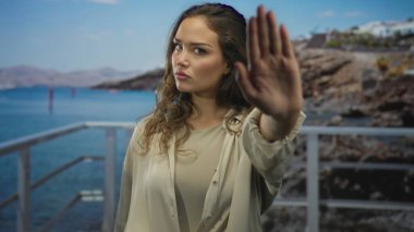 Ciddi ifadeli bir kadın, deniz kenarındaki gezinti sahasında durmak için avucunu uzatıyor; meydan okuma reddi sınırı.