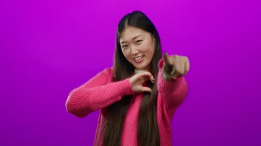 Pembe kazak giymiş, elleri ile kalp şeklinde gülümseyen genç, Asyalı, dışlanmış, dışa dönük, yetişkin, oyuncu bir kadının yer aldığı canlı pembe bir duvara karşı sevgi ve pozitiflik taşıyan bir kadın..