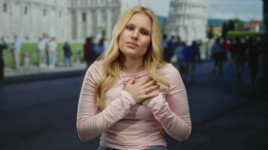 Kadın kendini rahatsız hissediyor, sidik kulesinin önünde göğsünü sıkıyor, turistlerle çevrili, ikonik italyan ortamında seyahat ederken sağlık endişelerini gösteriyor..