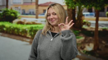 Parkta güzel bir jest yapan bir kadın. Parlak gülüşü olan, yemyeşil bir çevresi olan ve güneşli bir günde bulanık şehir geçmişi olan açık hava yaşam tarzını sergileyen bir kadın..