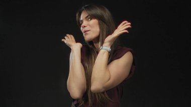 Genç İspanyol kadın neşeli bir şekilde gülümserken yüzünü izole edilmiş siyah bir arka planda gizliyor, neşeli, anlamlı bir ruh hali ve canlı bir etkileşimi somutlaştırıyor..