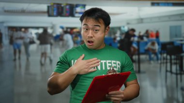 Kalabalık bir havaalanı terminalinde elinde bir pano tutan yeşil gömlekli genç adam arkasında bulanık gezginler olan bir iç mekanda örgütsel bir sahne sunuyor..