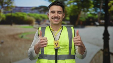 Yansıtıcı yelek giyen İspanyol adam güneşli bir park ortamında gönüllü ruhu ve açık hava toplum nişanını sembolize ediyor..
