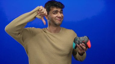 İspanyol genç oyuncu konsolun yanındaki stüdyoda oyun sahası kullanırken, adam kontrol cihazını kavrayıp arka planda baş parmağıyla işaret veriyor..