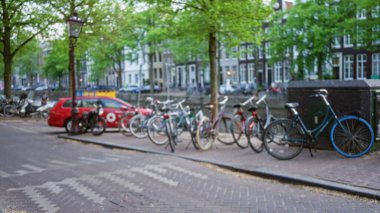 Bulanık bisikletler Hollanda, Amsterdam 'da bir kanalın kenarında yeşil yapraklı ağaçların altında tam anlamıyla bir Hollanda şehri manzarası sergiliyor..