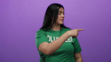 Bir jest yapan kadın, mor bir arka planı işaret ederek yeşil bir gönüllü gömleği giyip, kendine güvenini ve kendine güvenini ifade ederek oradan ayrılmak istiyor..