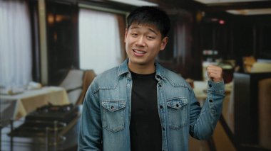 Kot ceketli genç adam şık bir restoranda şık bir dekor ve hafif ışıklandırmayla el kol hareketi yapıyor..