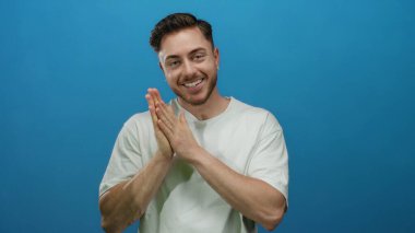 Sakallı genç adam sıcak bir şekilde gülümsüyor, parlak mavi bir arka plan karşısında beyaz gömlek giyiyor, dostça, yaklaşılabilir bir tavır sergiliyor, kurumsal veya yaşam tarzı için mükemmel..