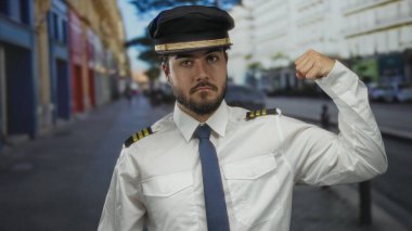 Sakallı, pilot üniforması ve şapkası olan genç bir adam şehrin bulanık arka planına karşı güç ve kararlılık hissini yakalıyor..