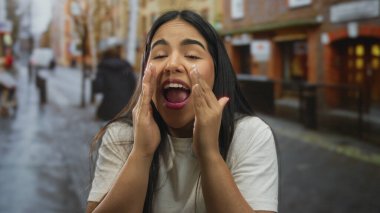 Kadın caddenin karşısındaki Latin kökenli genç bir arkadaşa seslenirken şehir zeminine gülümsüyor..