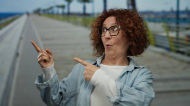 Orta yaşlı, esmer, kıvırcık saçlı ve gözlüklü bir İspanyol kadın deniz kenarında gezinirken heyecanla el kol geziyor, açık deniz ortamında sürpriz ve neşe saçıyor..