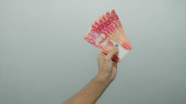 Filipinler 'in beyaz duvar arkaplanına karşı Filipin pesolarını elinde tutan beyaz adam, tarafsız bir ayar ile belirgin bir şekilde sergilenen Filipinler para birimi.