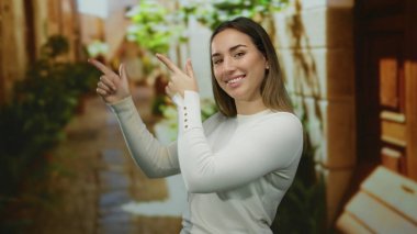 Beyaz kazaklı, yeşil yapraklı ve taş duvarlı, parmaklarıyla şehir caddesini gösteren bir kadın..
