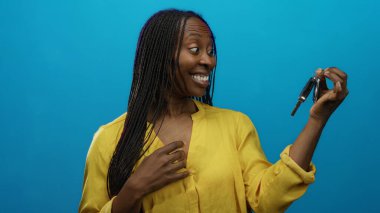 Gülümseyen ve elinde arabanın anahtarı olan bir kadın mavi izole edilmiş arka planda, yüzünde heyecan ve mutluluk olan sarı bir gömlek giyiyor..